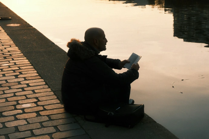 Man reading by the water at sunset